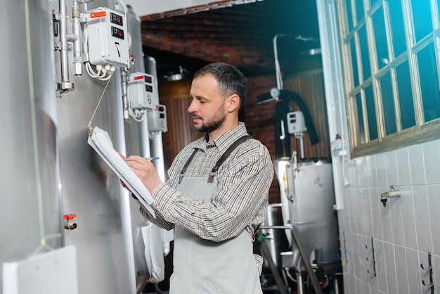 Un joven cervecero barbudo monitorea las lecturas del sensor durante el proceso de elaboración. Haciendo cerveza.