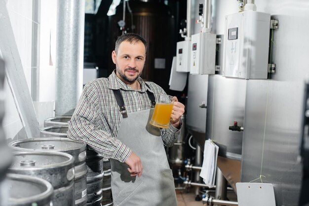 Un joven cervecero barbudo realiza el control de calidad de la cerveza recién elaborada en la cervecería.