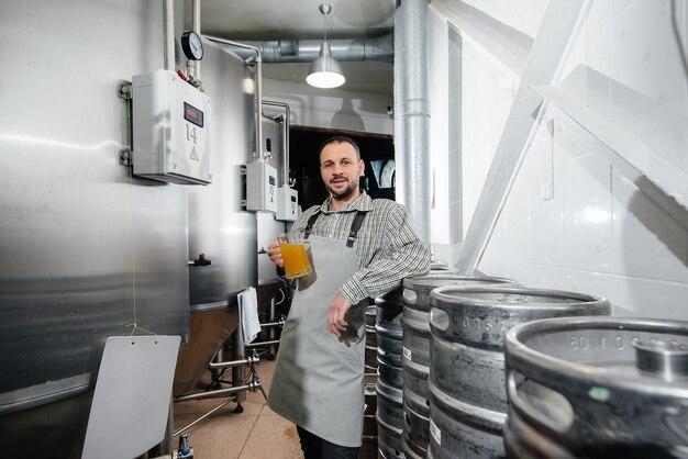 Un joven cervecero barbudo realiza el control de calidad de la cerveza recién elaborada en la fábrica de cerveza.