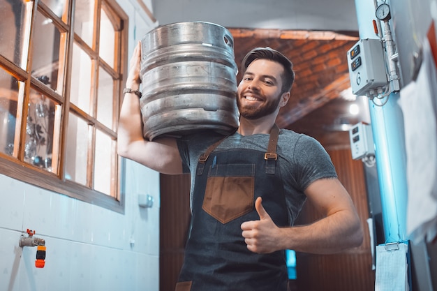 Foto un joven cervecero en un delantal sostiene un barril