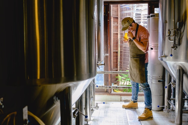 Joven cervecero sosteniendo un vaso de cerveza en la mano Echa un vistazo al sabor y el color de las cervezas en su cervecería artesanal