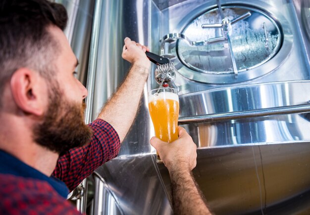 Joven cervecero vistiendo un delantal de cuero está probando cerveza en una cervecería moderna