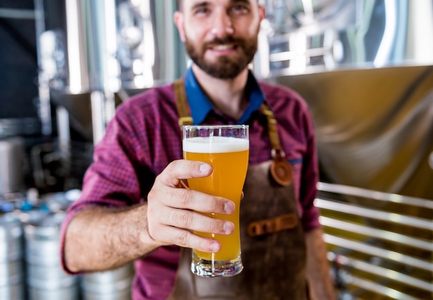 Joven cervecero vistiendo un delantal de cuero está probando cerveza en una cervecería moderna