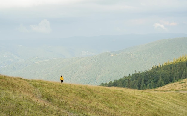 Un joven con una chaqueta amarilla camina en un prado con hierba amarillenta entre las montañas de vacaciones Imagen horizontal con espacio para tu diseño