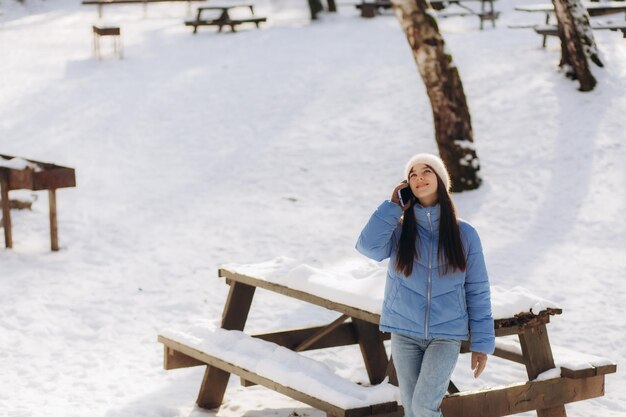 una joven con una chaqueta azul está hablando por teléfono en un parque de invierno