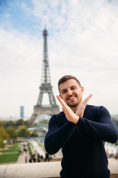 Un joven con una chaqueta azul oscuro está parado en el fondo de la Torre Eiffel. El clima soleado es otoño.