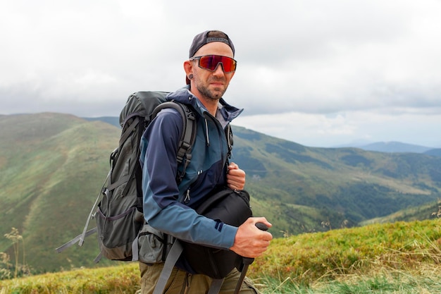 Un joven con chaqueta naranja y gafas se encuentra en la cima de la montaña con mochila