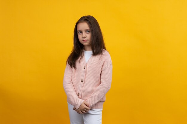 Una joven con una chaqueta rosa y jeans blancos posa sobre un fondo amarillo