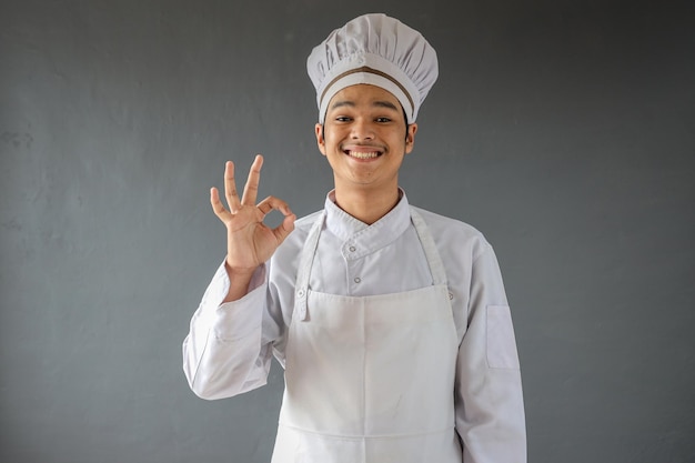 Joven chef asiático sonriente feliz con delantal blanco dando gesto de mano bien