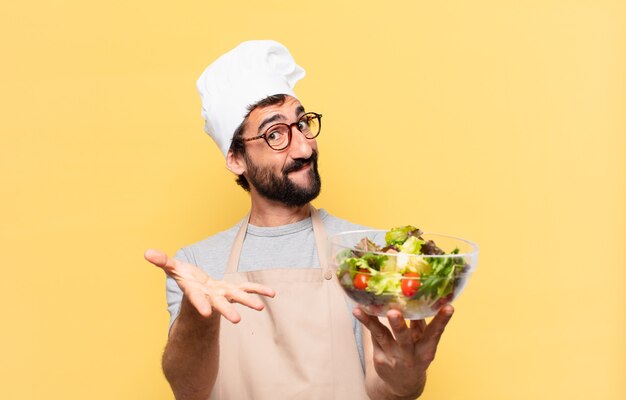 Joven chef barbudo feliz expresión y sosteniendo una ensalada