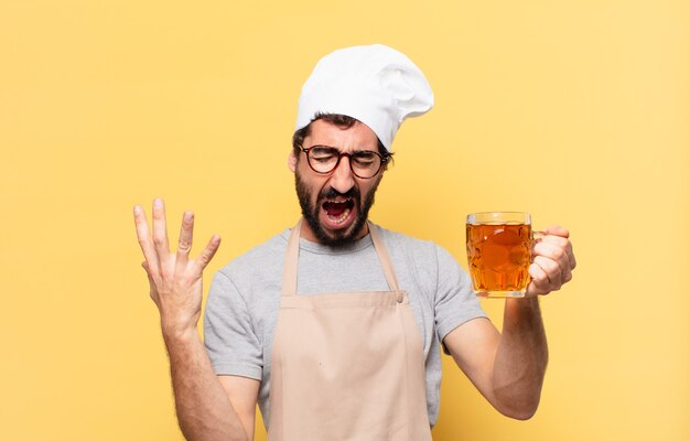 Joven chef barbudo hombre expresión enojada y sosteniendo una cerveza