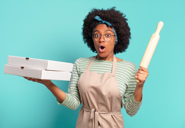 Joven chef bastante afro con un rodillo y pizzas