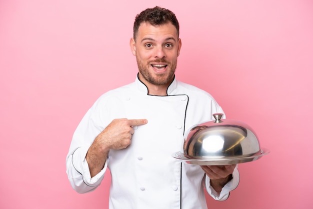 Joven chef brasileño con bandeja aislada de fondo rosa con expresión facial sorpresa