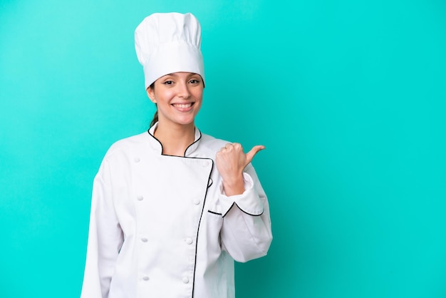 Joven chef caucásica mujer aislada de fondo azul apuntando hacia un lado para presentar un producto