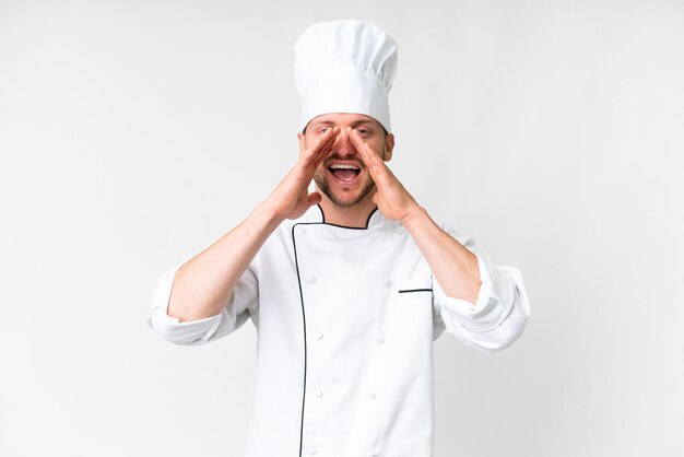 Joven chef caucásico sobre fondo blanco aislado gritando y anunciando algo