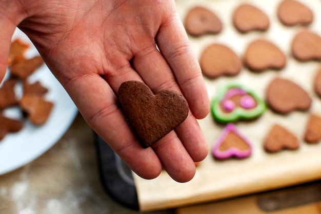 Un joven chef decora las galletas de jengibre con glaseado rosa, dibuja los ojos y la boca. Concepto de horneado