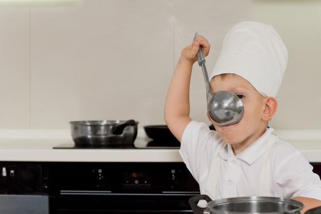 Joven chef degustación de sopa de cucharón en la cocina