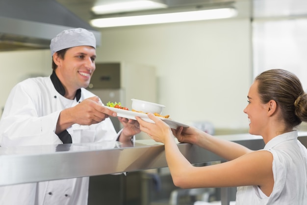 Joven chef feliz entregando un plato a la camarera