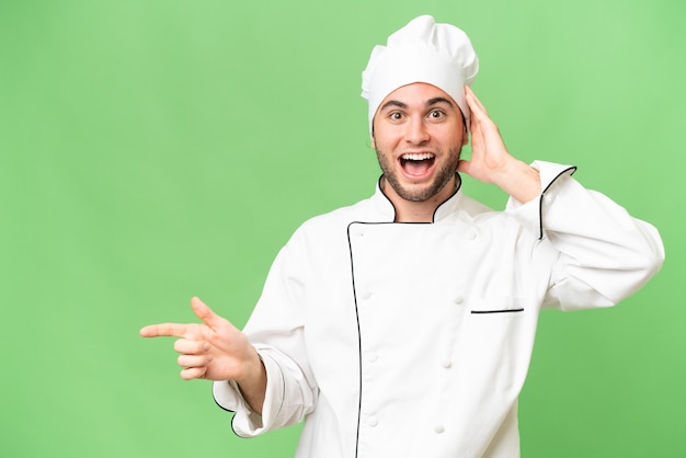 Joven chef guapo sobre un fondo aislado sorprendido y señalando con el dedo hacia un lado