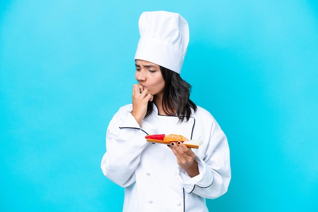 Joven chef hispana mujer sosteniendo sashimi aislado sobre fondo azul con dudas