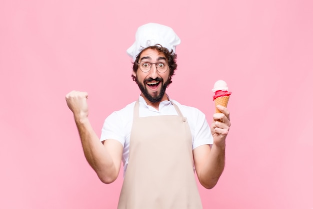 Joven chef loco con un helado contra la pared rosa