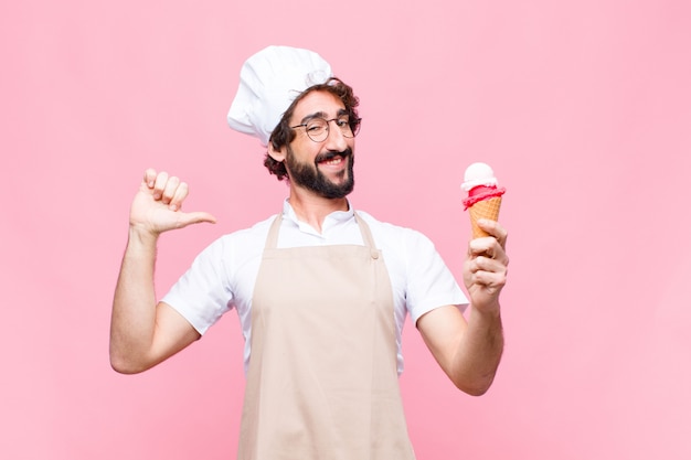 Joven chef loco con un helado en la pared rosa