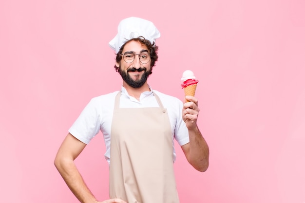 Joven chef loco con un helado en la pared rosa