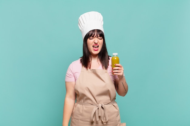 Joven chef mujer gritando agresivamente, luciendo muy enojado, frustrado, indignado o molesto, gritando no