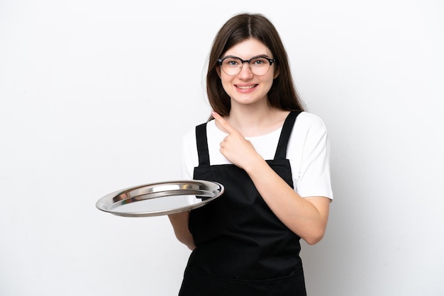 Joven chef rusa con bandeja aislada de fondo blanco apuntando hacia un lado para presentar un producto