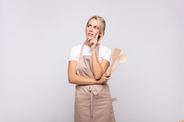 Joven chef sonriendo felizmente y soñando despierto o dudando, mirando hacia el lado