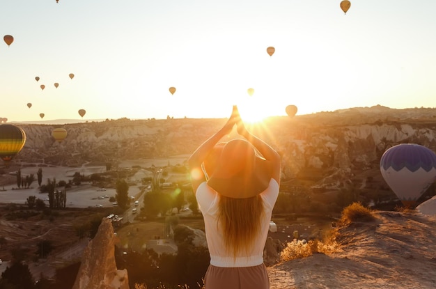 Joven chica atractiva de pie en la montaña con globos de aire volando en el fondo Capadocia