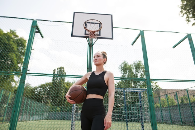 Joven chica deportiva con una pelota de baloncesto en la cancha de baloncestro al aire libre fin de semana activo