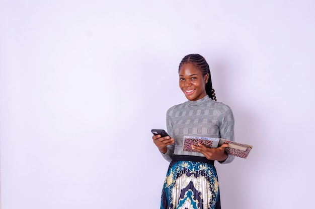 Joven chica divertida mujer de etnia afroamericana estudiante sostiene libros usa teléfono celular móvil aislado sobre fondo completamente blanco