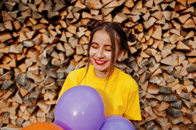 Joven chica divertida con ropa de maquillaje brillante en camisa amarilla con globos de colores sobre fondo de madera