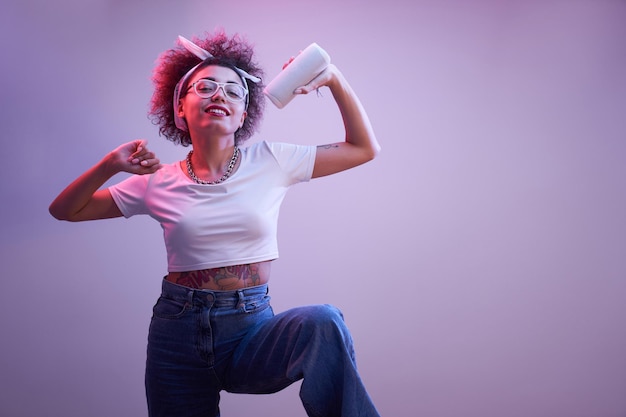 Joven chica kazaja positiva con peinado afro escucha música en bailes de altavoces portátiles y posa estilo hip hop