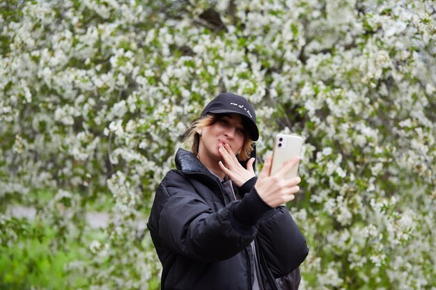 Joven chica milenaria con estilo que se toma una selfie bajo un cerezo en flor en la naturaleza primaveral que se conecta con el estilo de vida de autodescubrimiento de la naturaleza