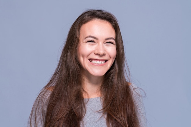 Joven chica positiva con cabello largo oscuro sobre un fondo azul.