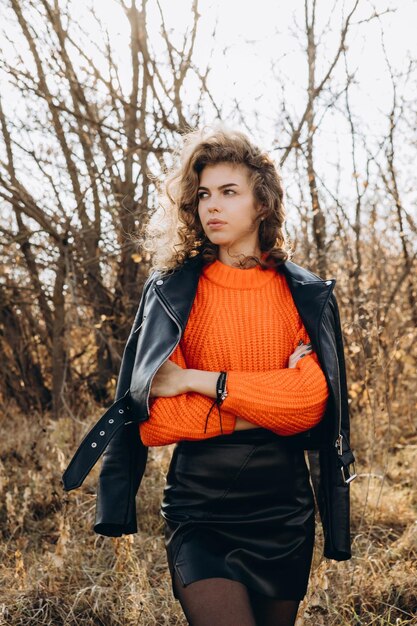 Joven chica rizada con un suéter naranja contra el telón de fondo de la naturaleza de otoño