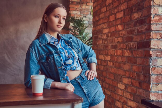 Una joven chica sexy delgada en una chaqueta de jeans y camisa de franela leani