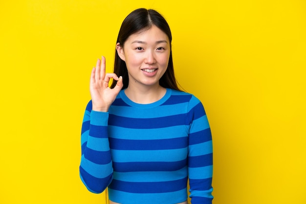 Joven china aislada de fondo amarillo mostrando el signo de ok con los dedos