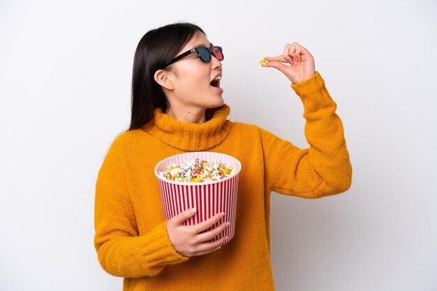 Joven china aislada de fondo blanco con gafas 3d y sosteniendo un gran cubo de palomitas de maíz