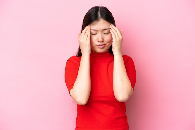 Joven china aislada de fondo rosa con dolor de cabeza