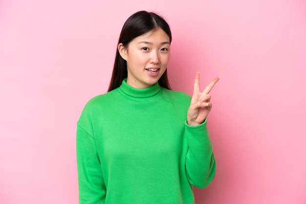 Joven china aislada de fondo rosa sonriendo y mostrando el signo de la victoria