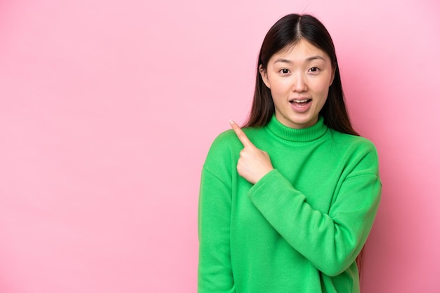 Joven china aislada de fondo rosa sorprendida y apuntando hacia el lado