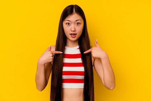 La joven china aislada en la pared amarilla apunta hacia abajo con los dedos, sentimiento positivo.