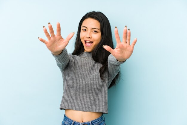 Joven China aislada en una pared azul se siente confiada dando un abrazo