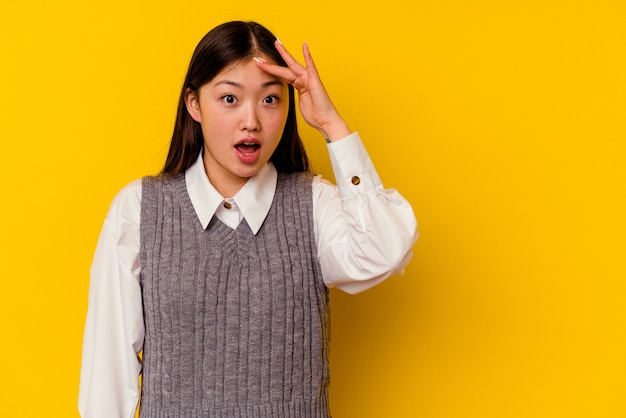 Joven china aislada sobre fondo amarillo grita fuerte, mantiene los ojos abiertos y las manos tensas.