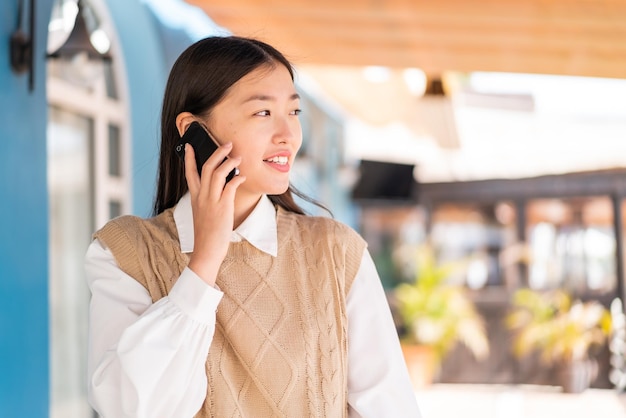 Joven china al aire libre manteniendo una conversación con el teléfono móvil con alguien