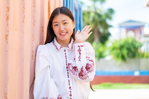 Joven china al aire libre saludando con la mano con expresión feliz