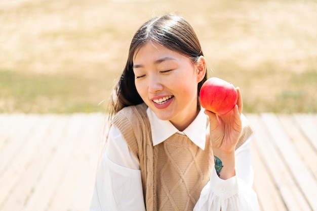 Joven china al aire libre sosteniendo una manzana con expresión feliz